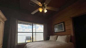 A bedroom with a large window, a bed, a ceiling fan, and wooden walls. - Leisure Lake Cabin, Toledo Bend Lake (Many)