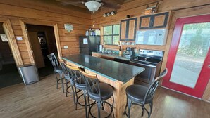 A wooden cabin interior with a kitchen island, bar stools, and a red-framed door. - Leisure Lake Cabin, Toledo Bend Lake (Many)