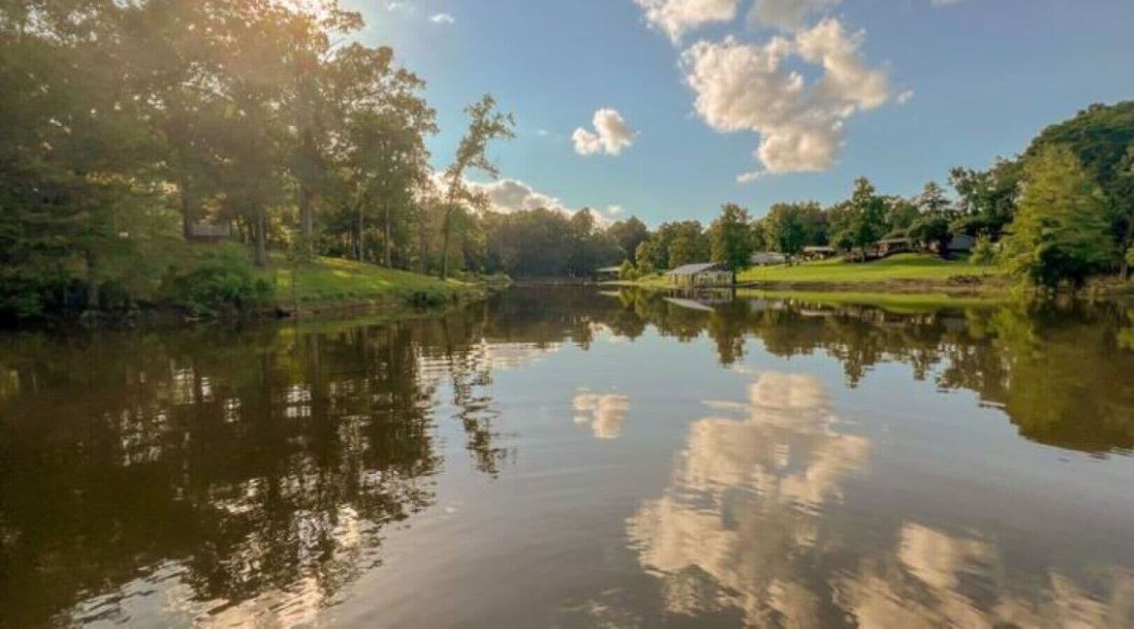 Um lago calmo refletindo árvores e um céu claro.