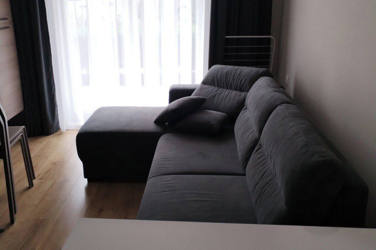 A modern room with a grey sofa, a small table, and a window with sheer curtains.