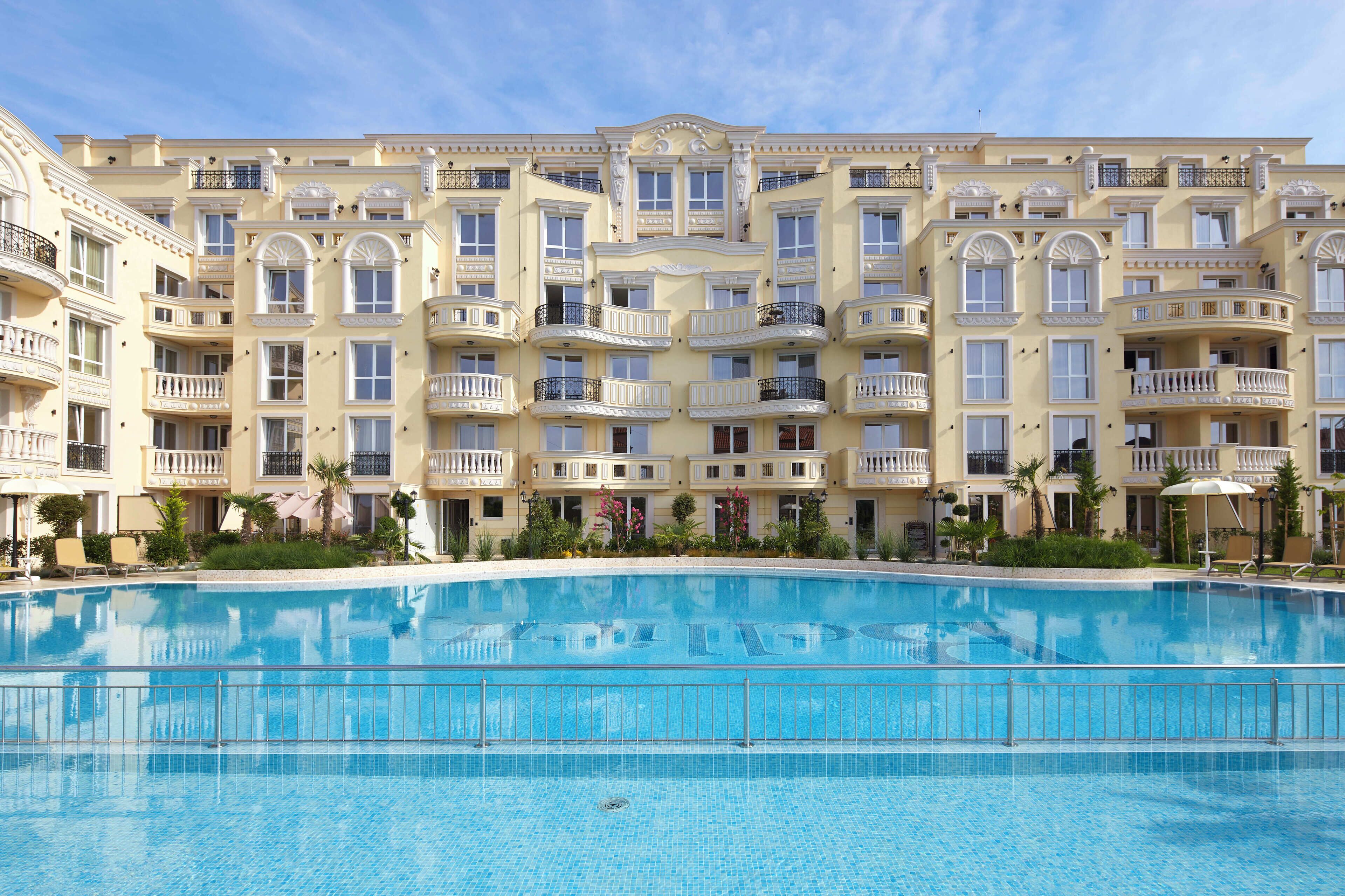 A large, clear swimming pool with a multi-story hotel building in the background.
