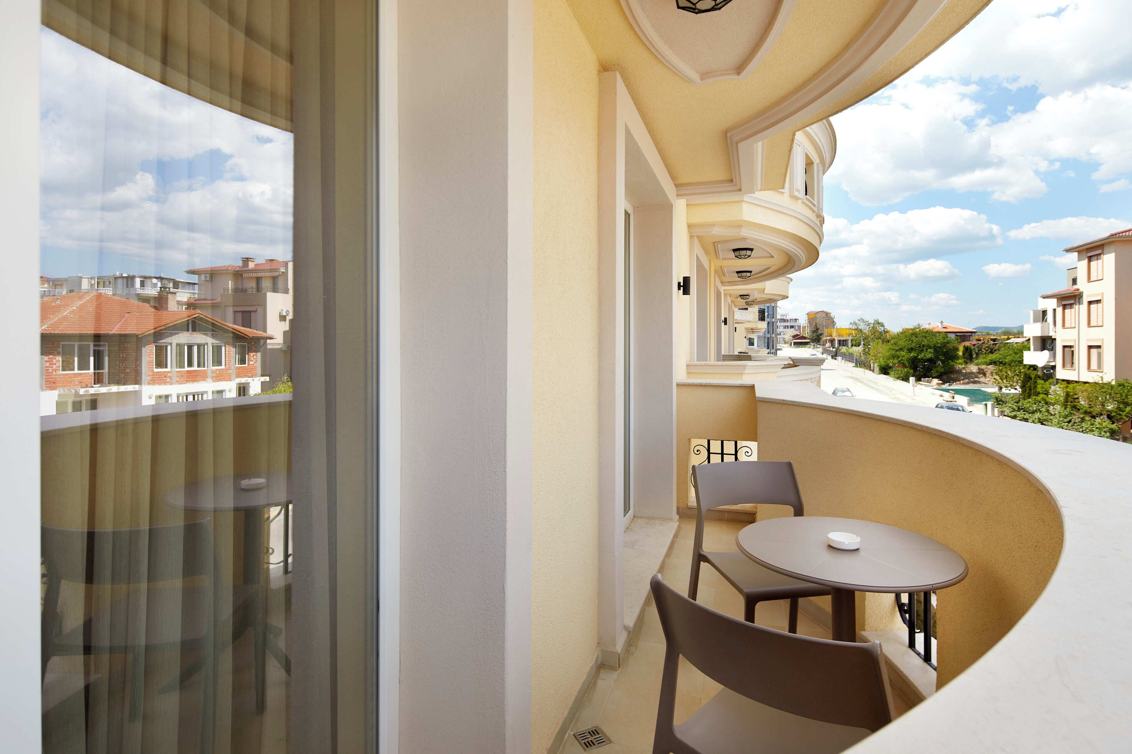 Ein Balkon mit rundem Tisch und Stühlen, Blick auf benachbarte Gebäude und einem geschwungenen architektonischen Design.