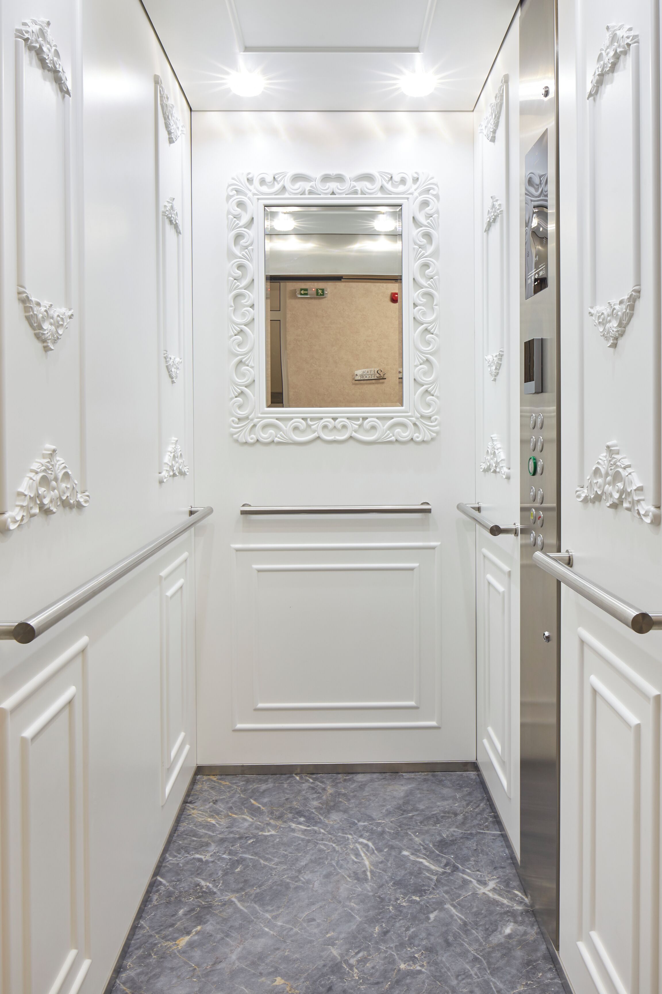 A narrow hallway with white walls, a marble floor, and ornate white door frames.