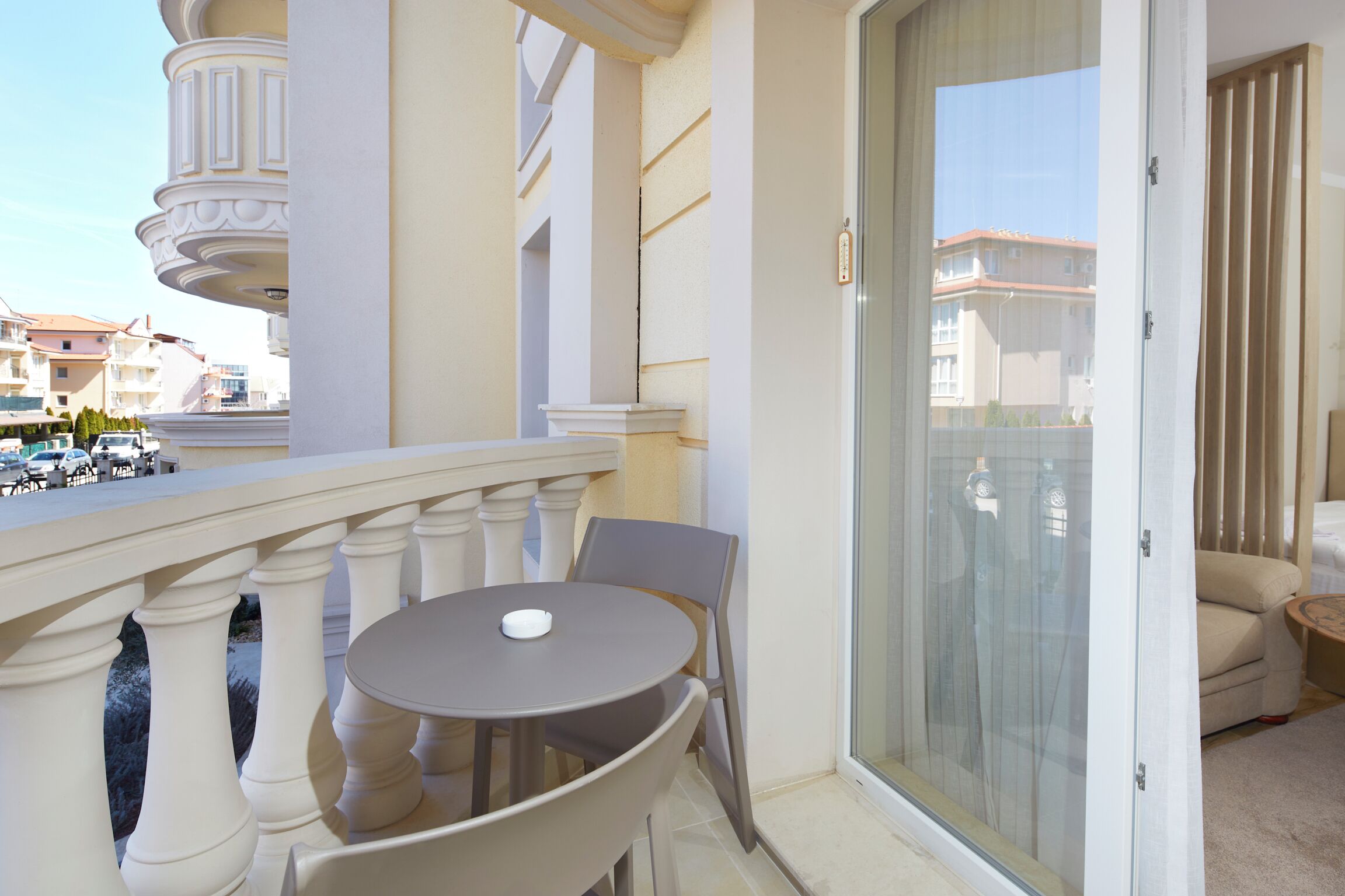 A balcony with a round table and chairs, a sliding glass door, and a view of other buildings.