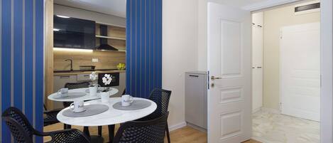 A compact kitchen with modern appliances, a dining area with a round table and chairs, and a white door leading to a bathroom.