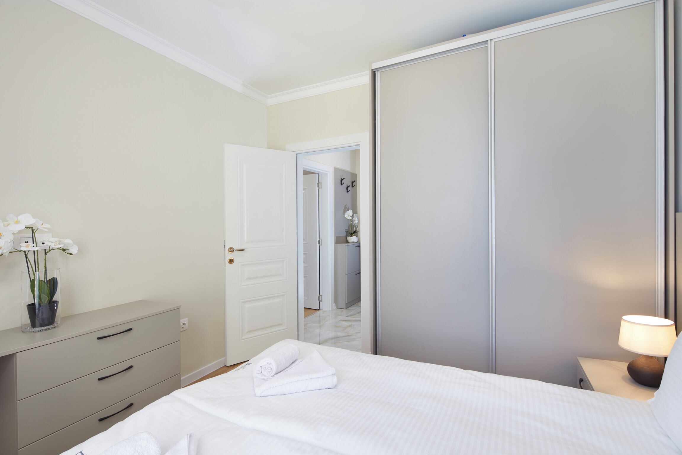 A bedroom with a bed, a nightstand with a lamp, a dresser, and a wardrobe.