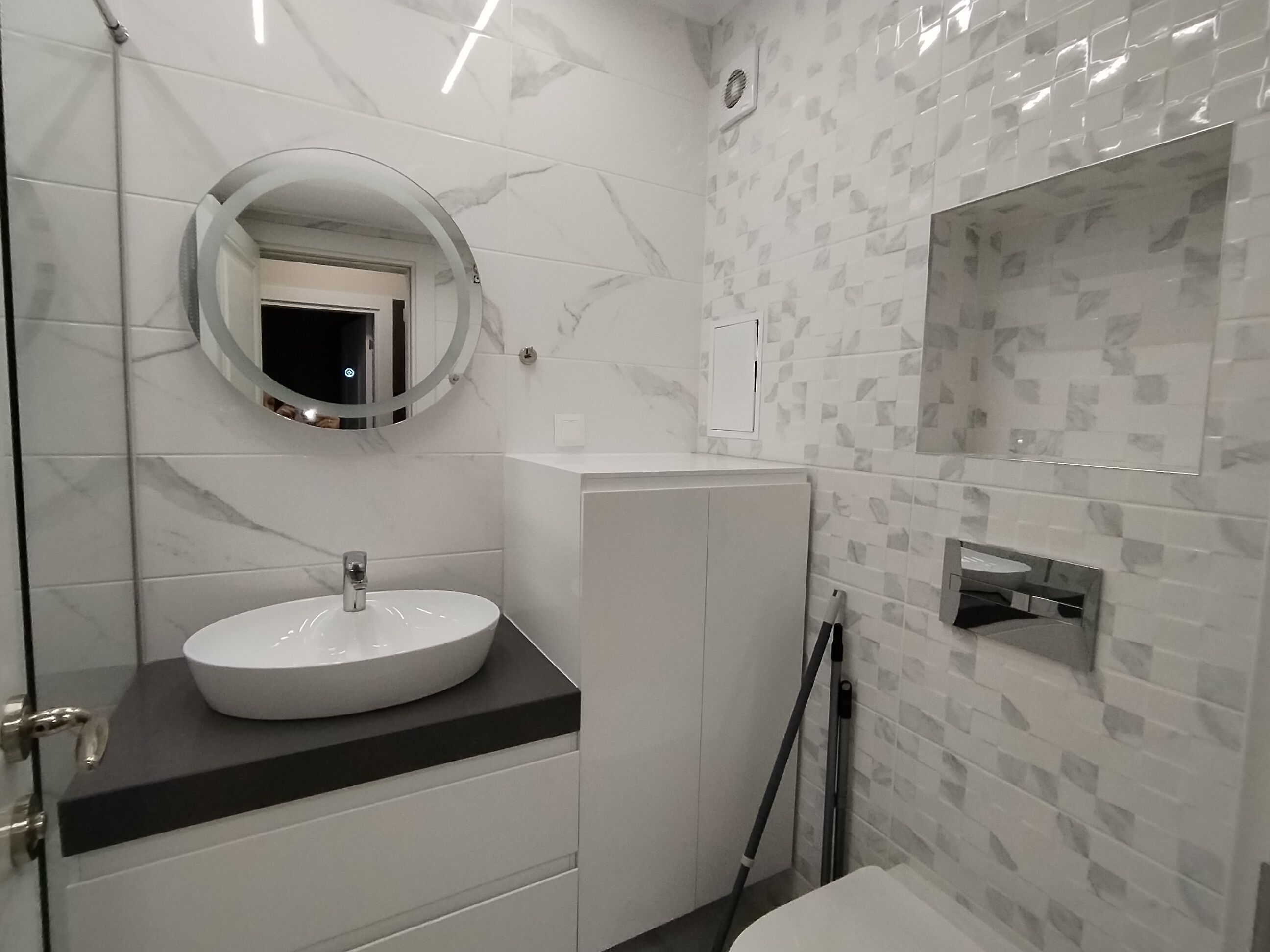 A modern bathroom with a round mirror, a sink, a shower, and a toilet.