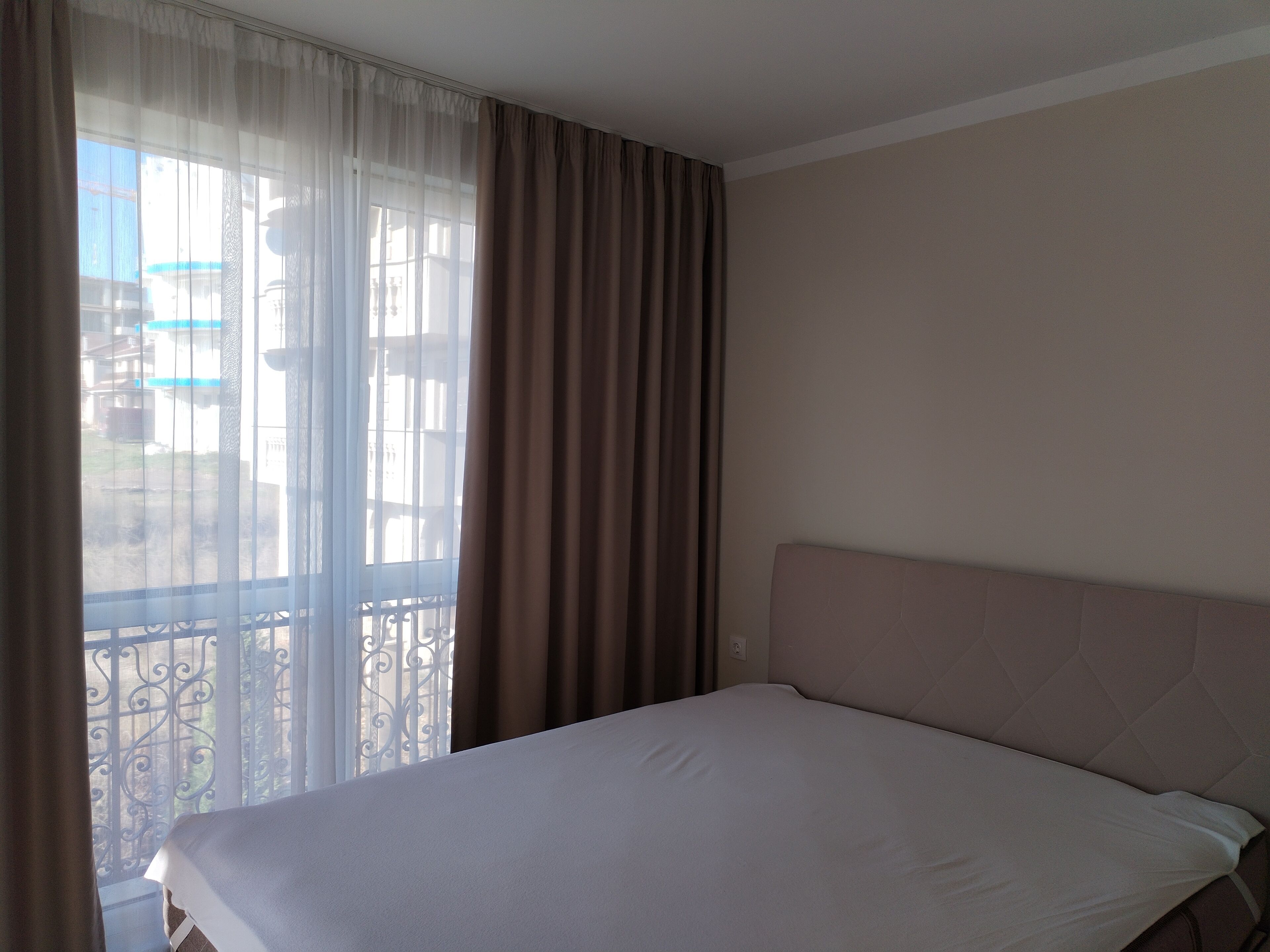Quarto de hotel com cama, cortinas e vista pela janela com varanda.