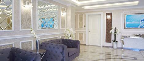 A spacious lobby with a grey sofa, a small table, and a large TV on the wall.
