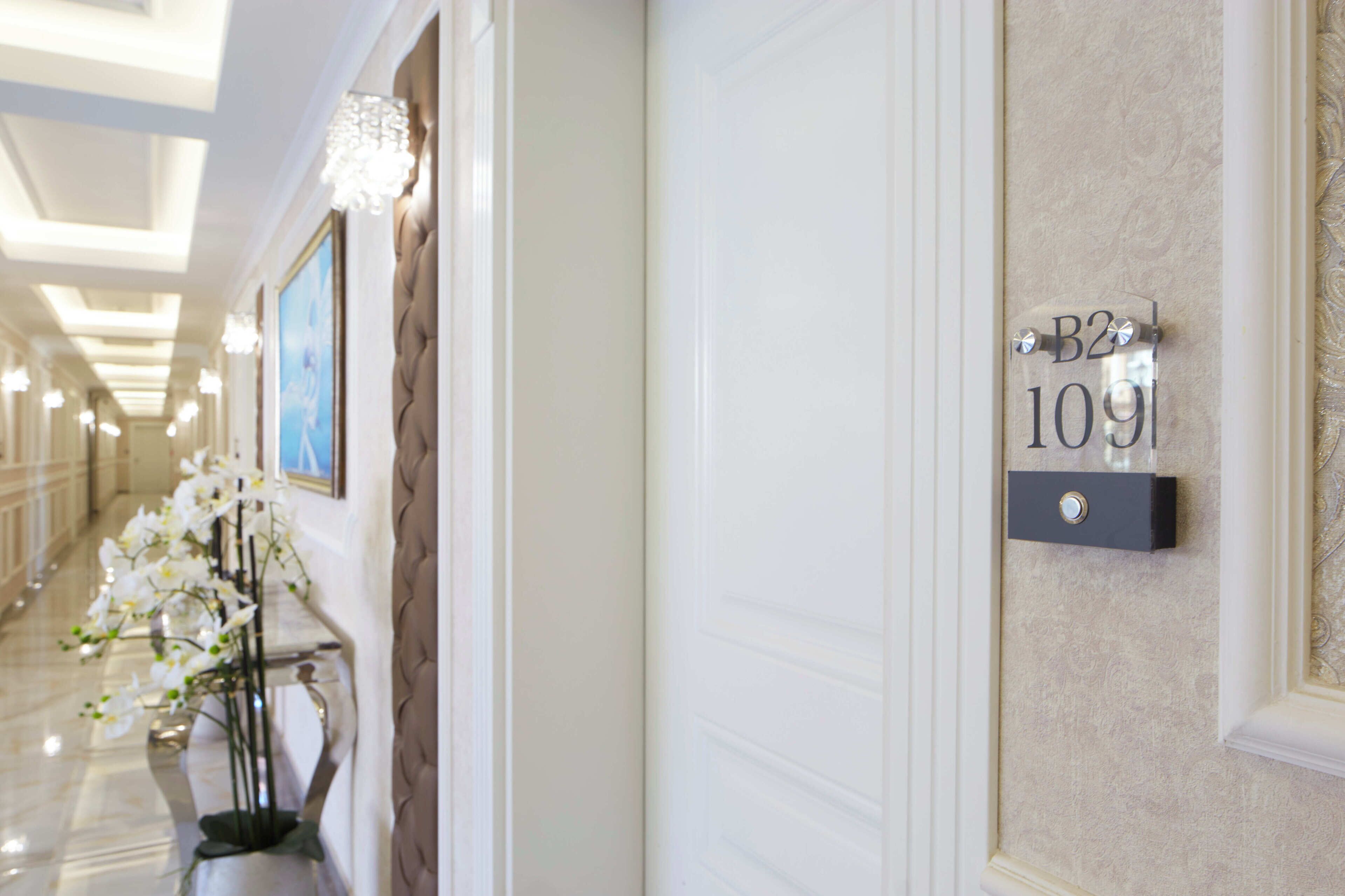 A hallway with a sign reading "B2 109" on the wall, a vase with white flowers, and a framed picture on the wall.