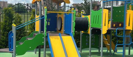 A playground with a yellow slide, green climbing area, and a blue and yellow climbing structure.