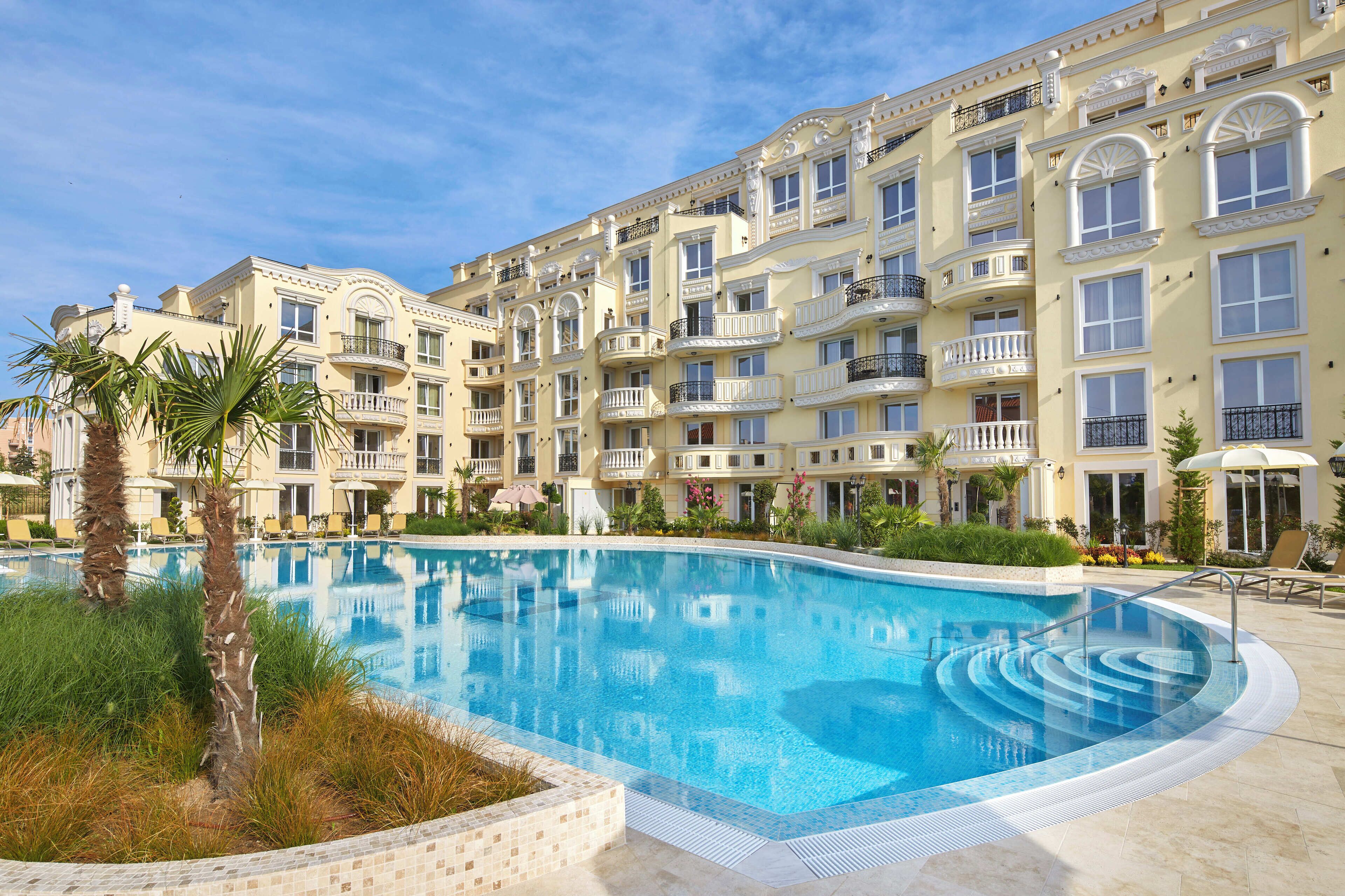 A multi-story hotel with a swimming pool surrounded by palm trees and lounge chairs.