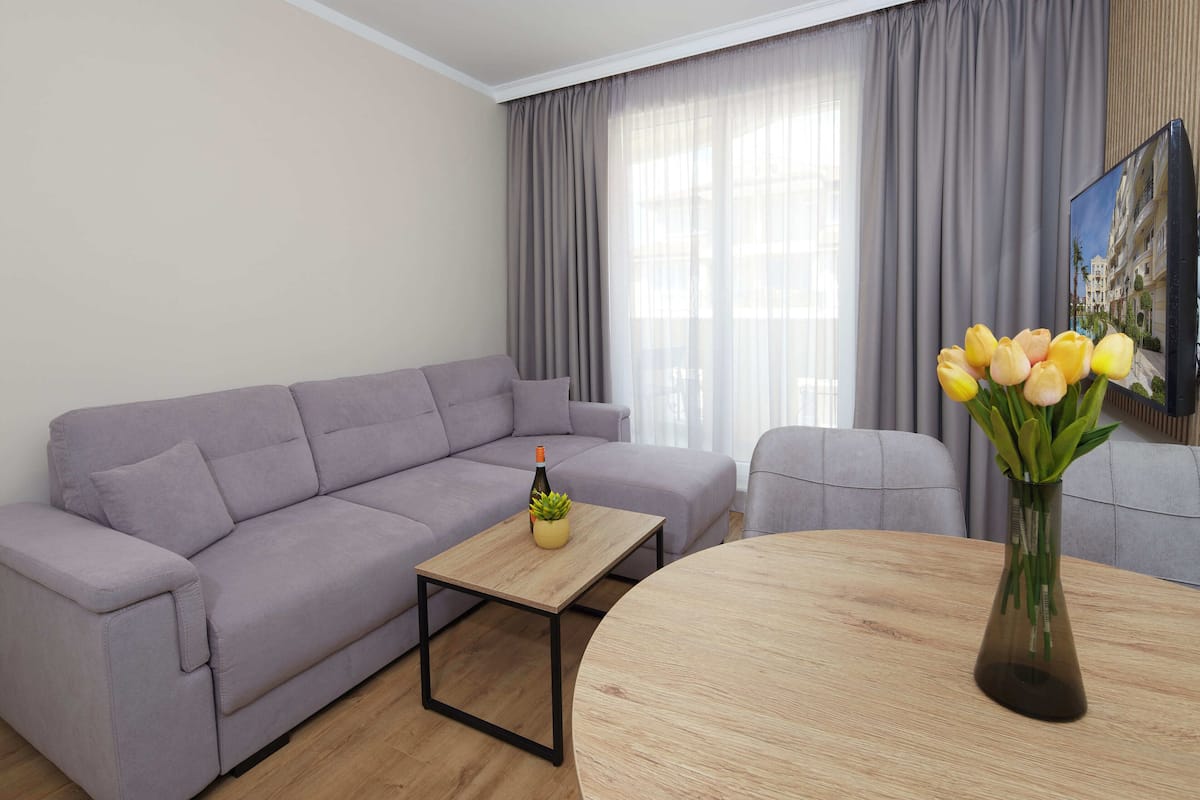 A modern living room with a grey sofa, a wooden coffee table, and a vase with yellow flowers.