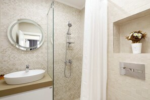 A bathroom with a round mirror, a shower, a sink, and a vase with flowers on the wall.