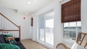 Un salon moderne avec un canapé noir, un plaid vert et un fauteuil en osier.