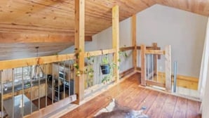 Quarto espaçoso com piso de madeira, teto alto e varanda com grade.
