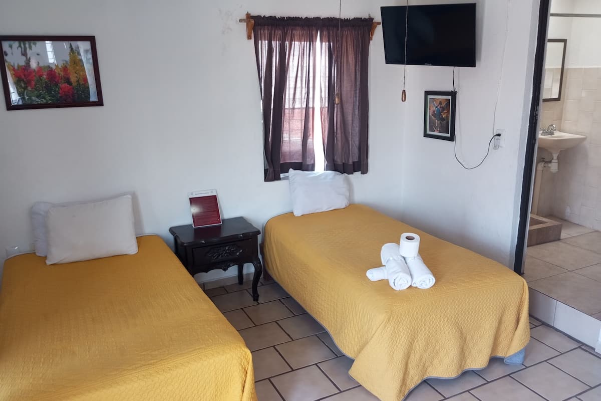 A hotel room with two beds, a TV, a small table with a red object, and a bathroom visible through an open door.