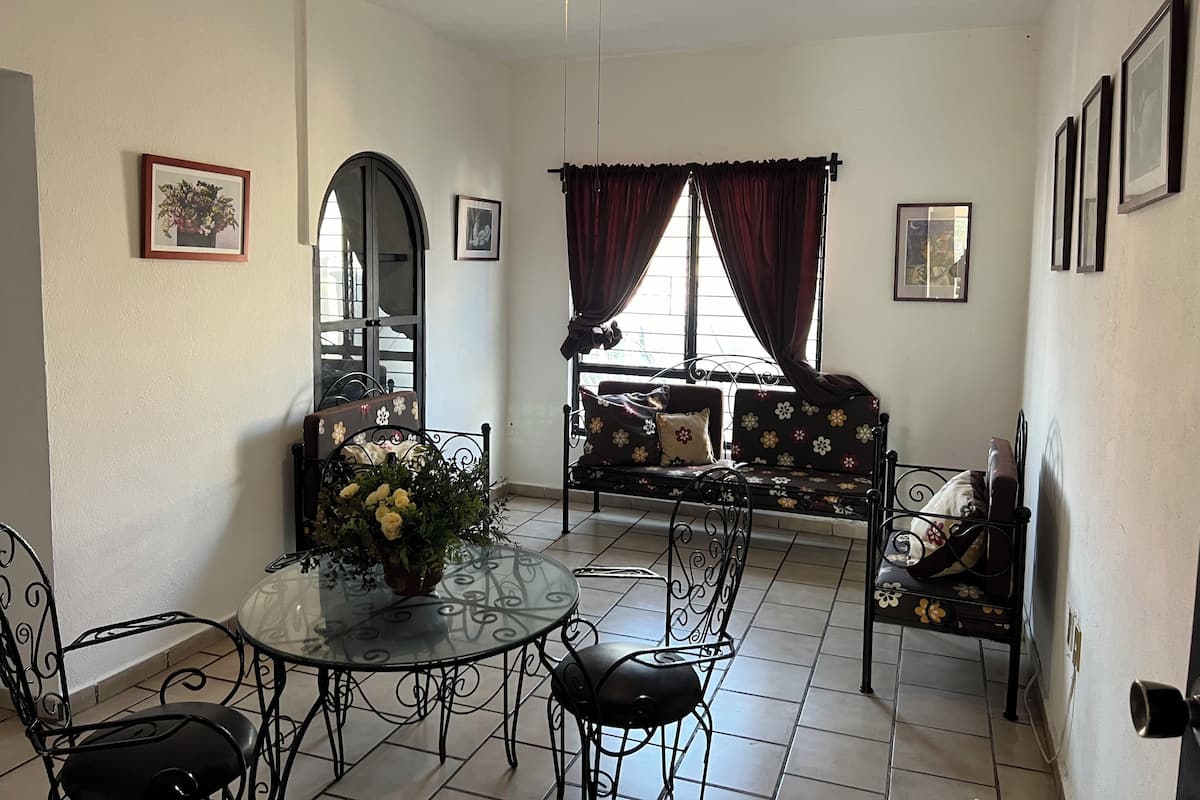A dining area with a glass table, black metal chairs, a sofa with floral upholstery, and a ceiling fan.