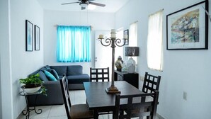 A dining area with a table and chairs, a ceiling fan, a blue curtain, and a framed picture on the wall. - Casa Los Angeles  (Colima)
