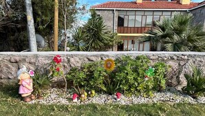 Un jardín con estatuas decorativas, un muro de piedra y un edificio con techo de tejas rojas al fondo.