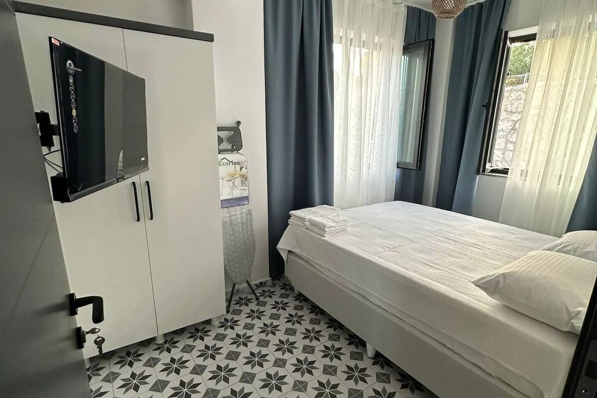 A bedroom with a bed, a wardrobe, a television, and a window with curtains.