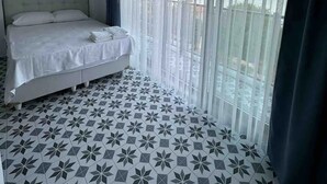Un dormitorio con cama, lámpara colgante, cortinas translúcidas y vistas al balcón.