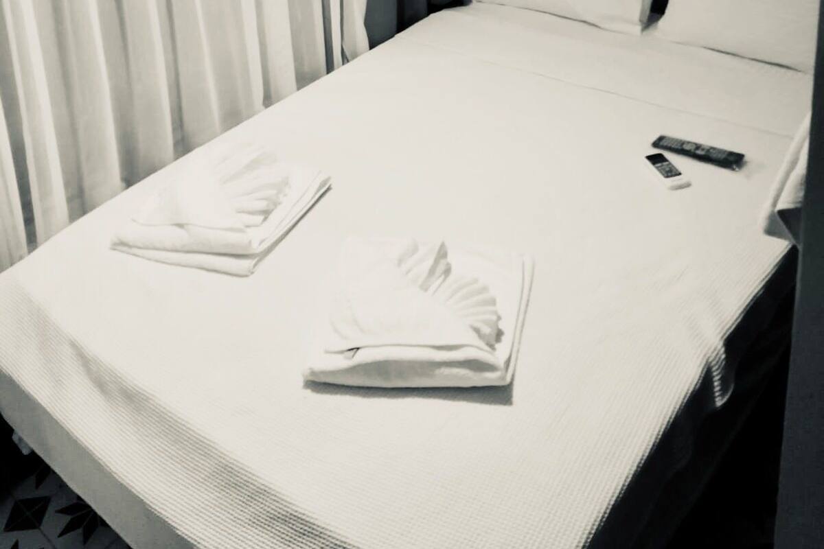 A neatly made bed with white linens, a remote control, and a folded towel on a hotel room bed.