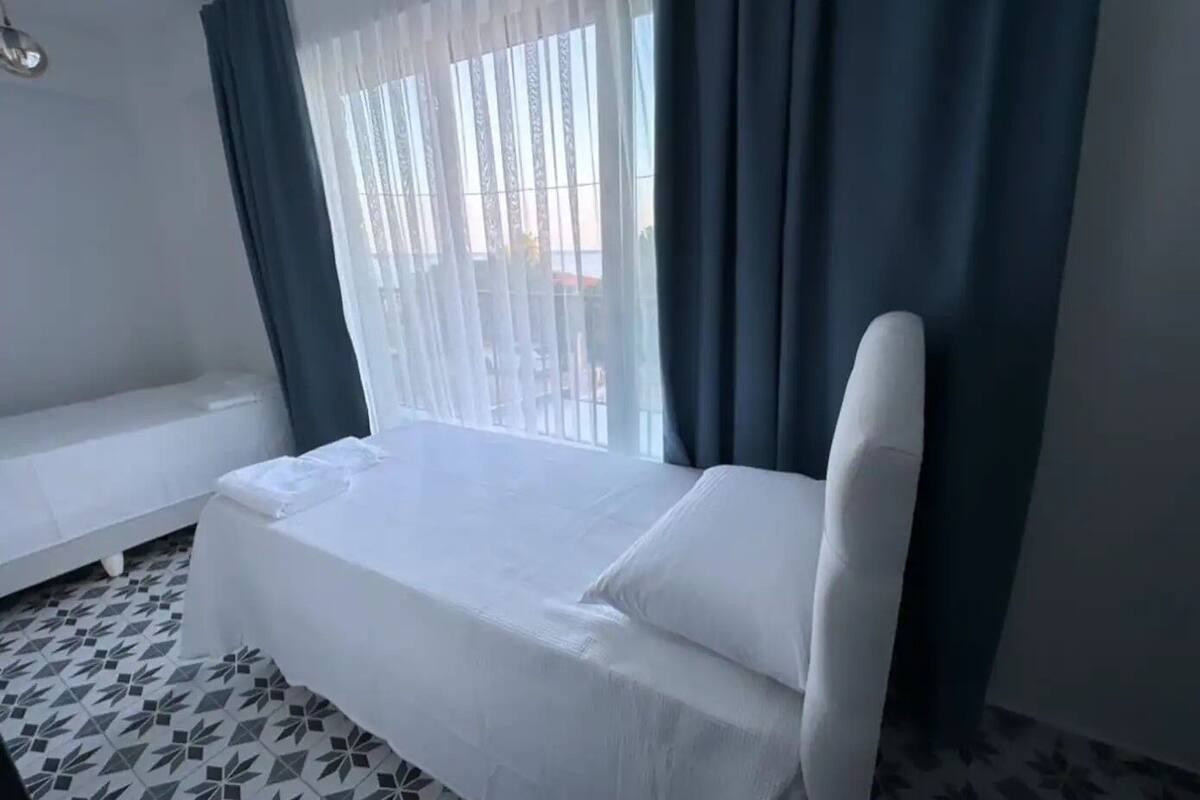 A single-bed room with a white bed, a bench, and a patterned floor.