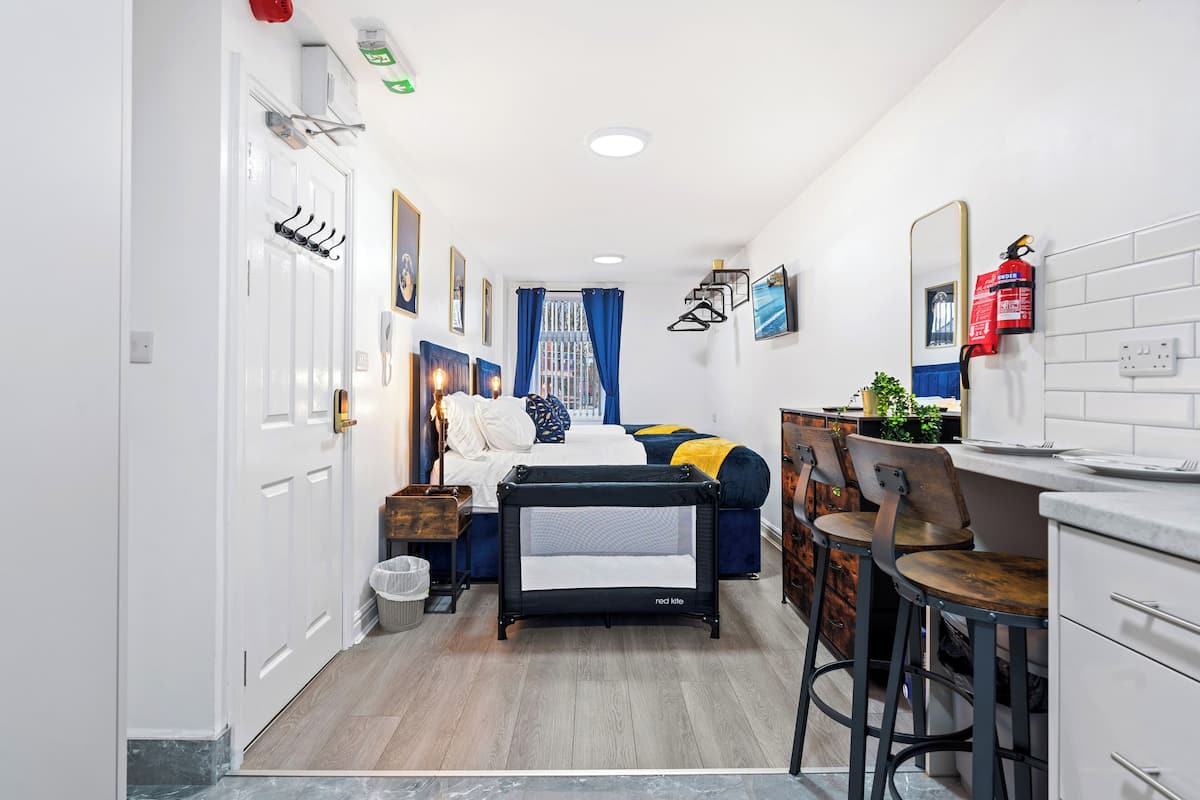 A compact hotel room with a bed, a small kitchenette, a seating area with a table and chairs, and a bathroom with a toilet and sink.