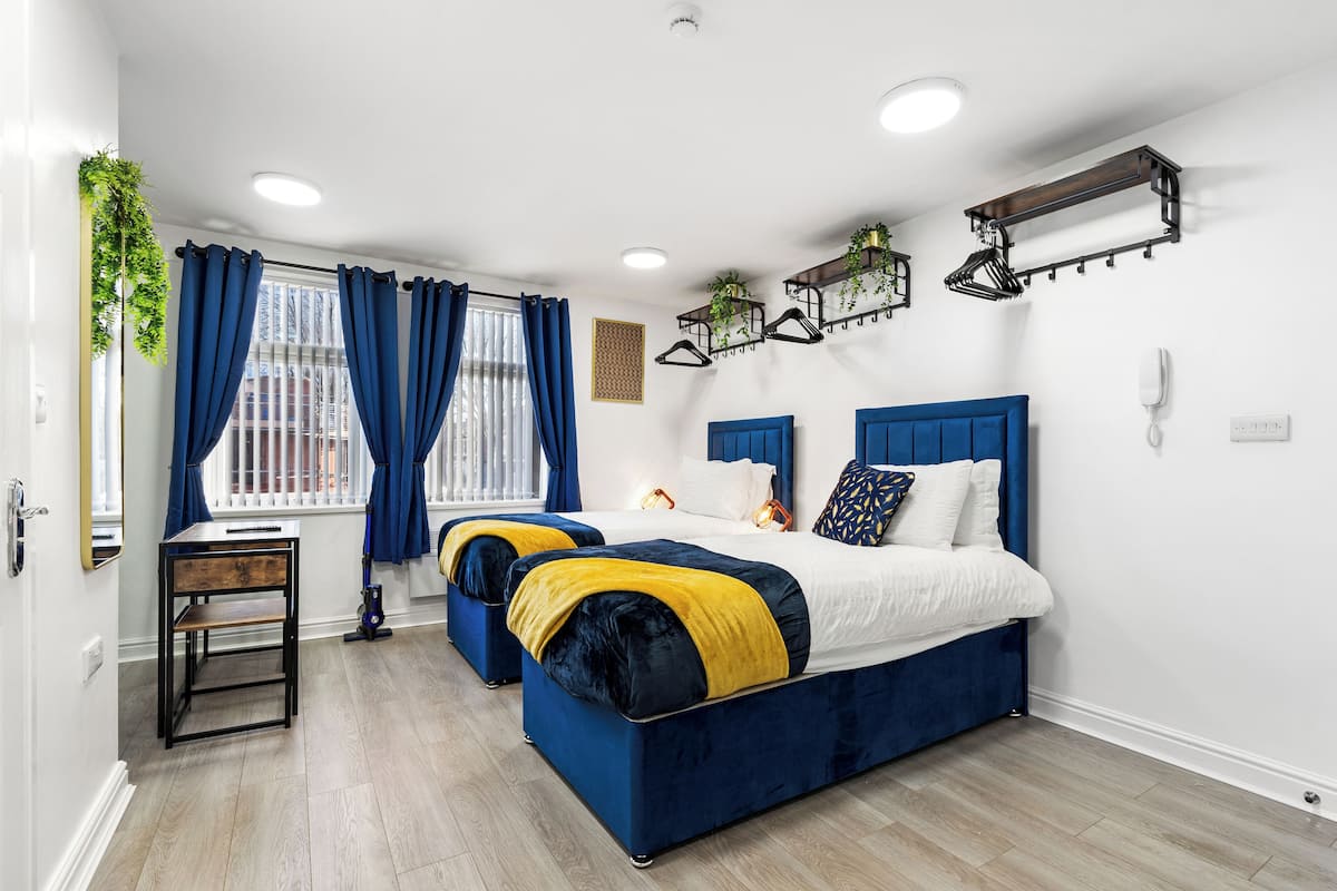 A bedroom with two beds, a desk, and a window with curtains.