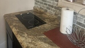 A kitchen with a stone backsplash, a black induction cooktop, a roll of paper towels, and a small potted plant on a shelf. - Tiny home for  short and long term also (Sugar Land)