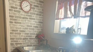 A kitchen with a brick wall, a clock, a window with curtains, and a sink. - Tiny home for  short and long term also (Sugar Land)