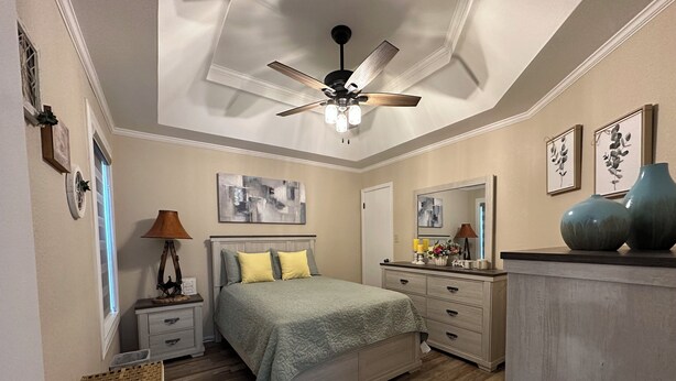 A bedroom with a bed, nightstands, a dresser, a ceiling fan, and artwork on the walls.