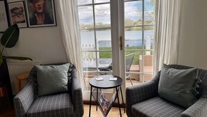 A room with two grey checkered sofas, a small round table, and a view of a lake through a glass door.