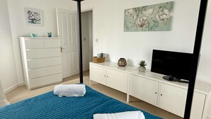 A bedroom with a bed, a TV, a wardrobe, and a painting on the wall.