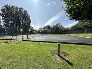 A fenced tennis court with a sign indicating it is part of a club. - Barnsley Turret House, set on the edge of the Windrush Lake (Windrush Lake)
