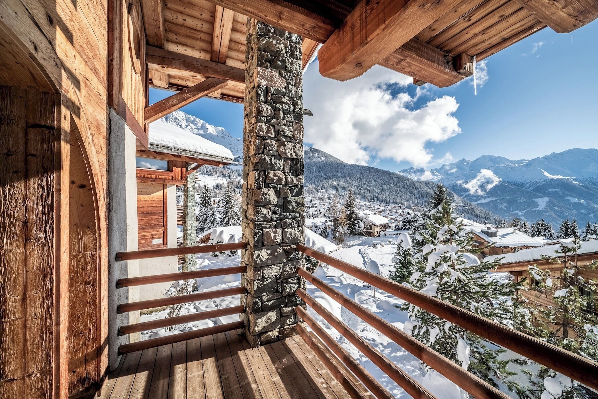 A wooden balcony with a stone pillar, overlooking a snowy mountain landscape.