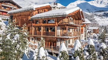 Een houten chalet met meerdere balkons, omringd door besneeuwde bomen en bergen.