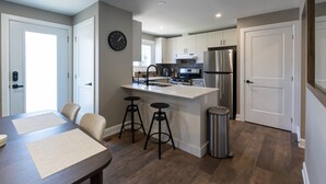 Een moderne keuken met een centraal eiland, barstoelen, een roestvrijstalen koelkast en een klok aan de muur.