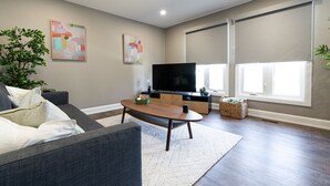 Een moderne woonkamer met een bank, salontafel, televisie en kunstwerken aan de muren.