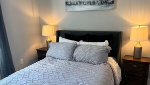 A bedroom with a large bed, two bedside tables with lamps, a headboard, and a painting on the wall. - Brand New Stylish Black Cottage (South Kingstown)