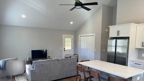 A modern kitchen with a central island, white cabinets, and a stainless steel refrigerator. - Brand New Stylish Black Cottage (South Kingstown)