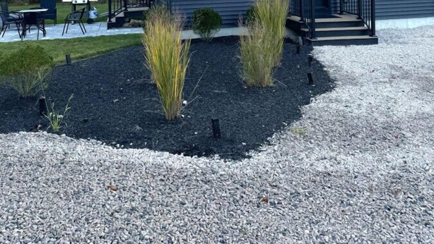 A modern, single-story building with a dark exterior, a front porch, and a gravel driveway. - Brand New Stylish Black Cottage (South Kingstown)