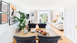 A dining area with a wooden table, chairs, and a view of a garden through a sliding door. - Broadway house, 3 bedroom and dog friendly (Windrush Lake)