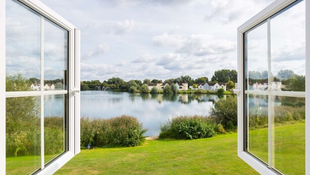 A view through a window of a lake with houses in the background. - Broadway house, 3 bedroom and dog friendly (Windrush Lake)