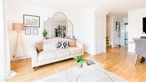 A living room with a sofa, a coffee table, and a lamp. There is a mirror and a door leading to another room. - Broadway house, 3 bedroom and dog friendly (Windrush Lake)