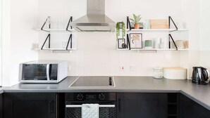 A modern kitchen with a built-in microwave, stove, and oven. There are shelves with decorative items and a small plant. - Broadway house, 3 bedroom and dog friendly (Windrush Lake)