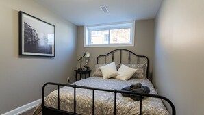 A bedroom with a bed, a window, a framed picture on the wall, and a nightstand with a lamp. - Cozy 2BDR Lots Of Amenities (Cornwall)