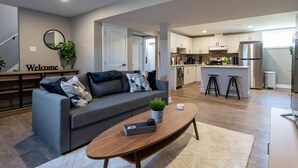 A modern living room with a grey sofa, a coffee table, and a "Welcome" sign on the wall. - Cozy 2BDR Lots Of Amenities (Cornwall)