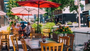 An outdoor cafe with tables and chairs under striped umbrellas, surrounded by greenery and buildings. - Cozy 2BDR Lots Of Amenities (Cornwall)
